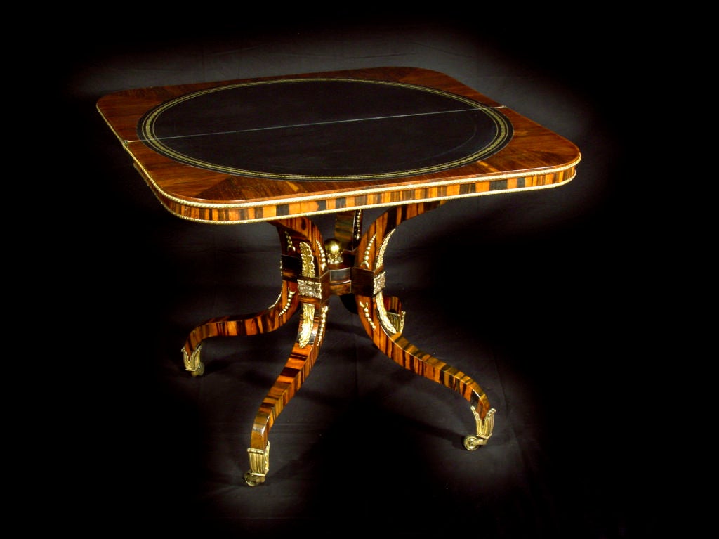 The top with rounded corners and rosewood crossbanding inset with brass fleur de lys; raised on four incurving legs joined by a finial-mounted stretcher and ending in leaf cast brass castors.