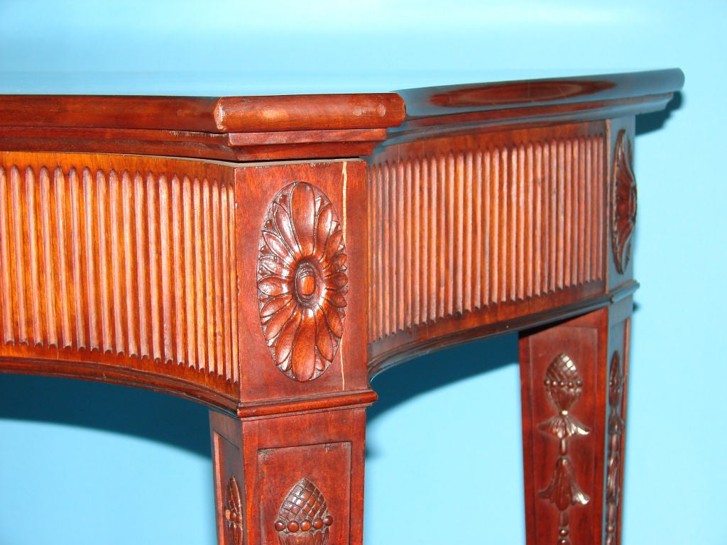 A fine pair of Irish George III style mahogany console tables made and signed by J. Hicks, Pembroke Street (Dublin). The serpentine tops above a fluted frieze centered by an urn, raised on square tapered legs carved with fir cones and bellflowers,