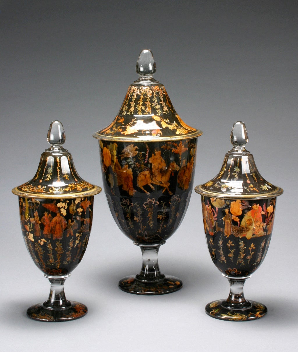 Each with a faceted cover surmounted by a finial, the conforming body raised on a footed circular base,decorated with chinoiserie figures and flowers on a black ground.<br />
<br />
<br />
This item @ H.M.Luther<br />
The Carlyle<br />
35 East