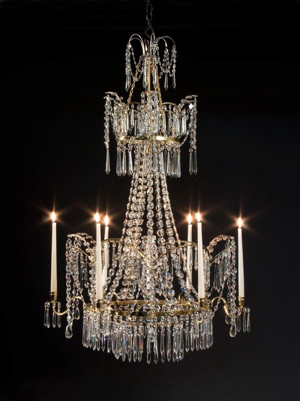 The two tiered corona fitted with arches hung with swags and faceted drops, the central cascade of graduated strands and feather sprays, the principal tier fitted with six S-shape arms supporting urn form candleholders alternating with arches