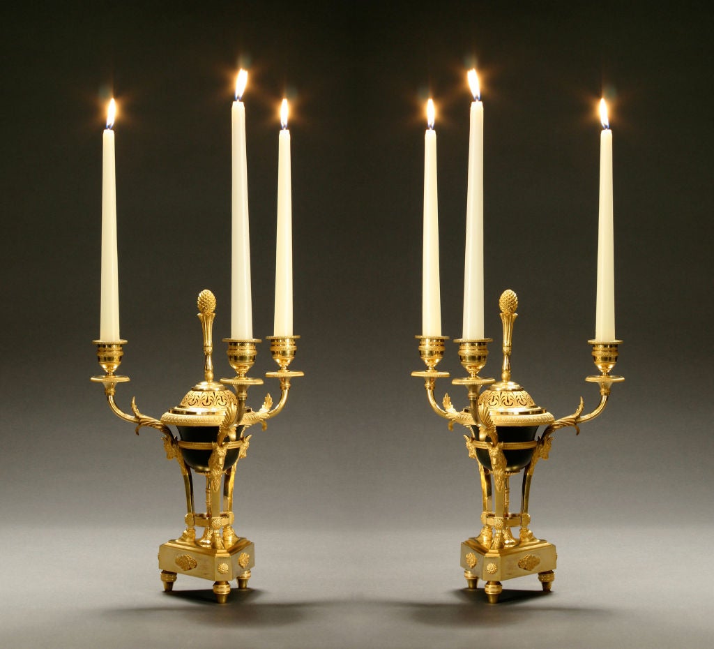 Each with a ram’s head monopodium tripod surmounted by a palm frond and pineapple finial, with three acanthus leaves issuing candle branches, on a triangular base with flower clasps above toupie feet.<br />
<br />
<br />
This item @ H.M.Luther