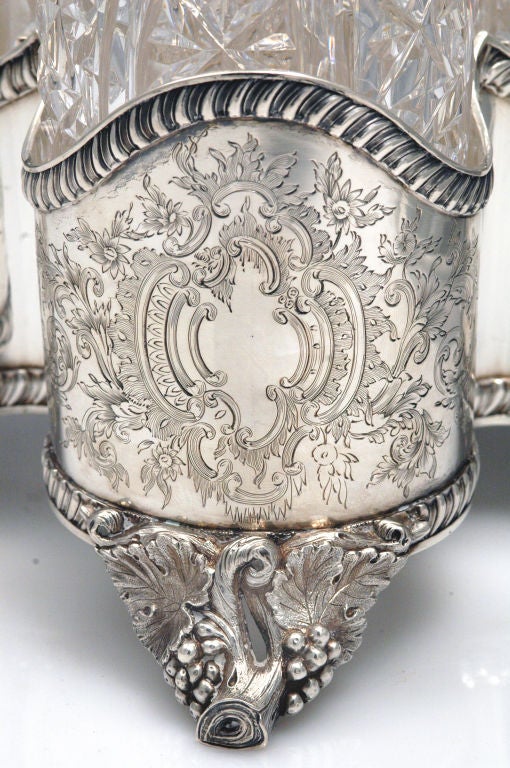 Coin silver four-bottle decanter stand by Lincoln & Foss of Boston, Mass., circa 1850 of quatrefoil shape with cast figural grapevine feet and matching central ring handle, the scalloped high sides engraved with rococo cartouches and gadroon