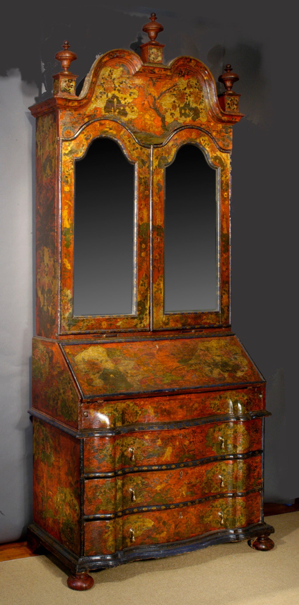 Rare early 18th century red chinoiserie decorated secretary bookcase, having a double arched pediment with three original finials, above a pair of arched mirrored doors enclosing a fitted interior with drawers and folio shelves, the slant front