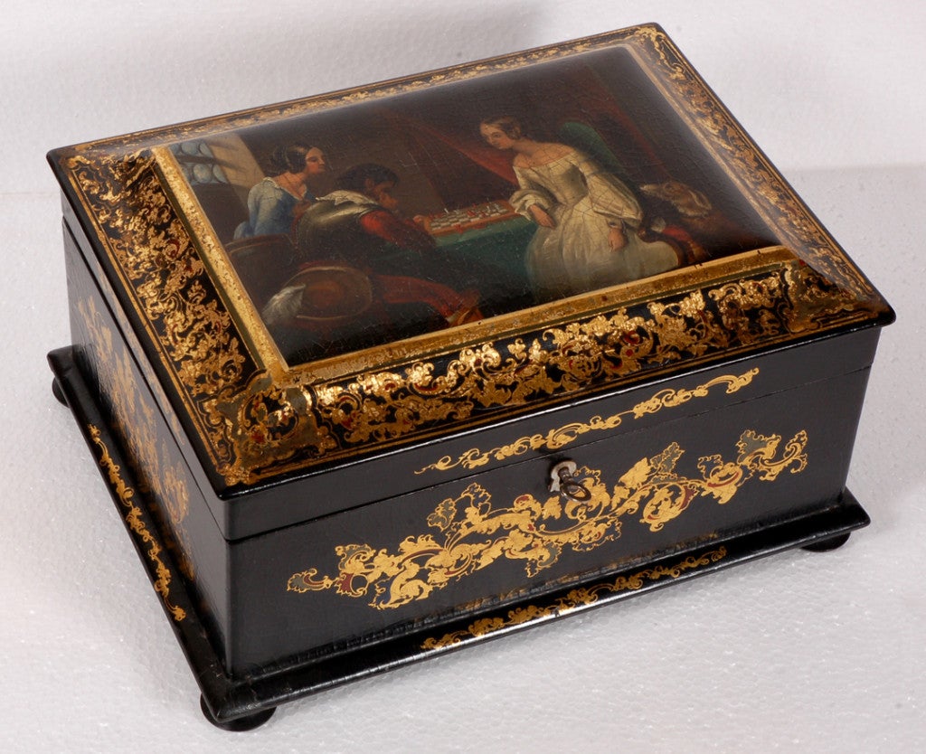 English black papier mache’  hinged lid box with lid painted with a scene of figures  playing chess, in  costume of the Romantique Revival framed in gilt scroll work. The interior is fitted with ivory and mother of pearl sewing tools.  England,