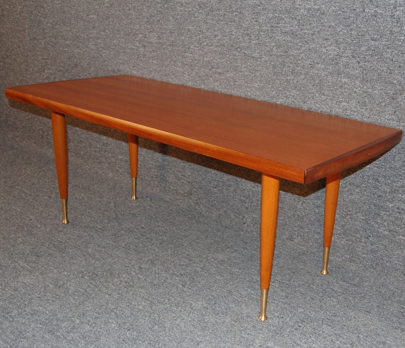 Sleek coffee table of rich natural teak.  Tapered legs with spun brass caps and feet.  Stamped underneath:  