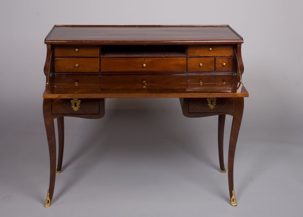 An important French Louis XV period, amaranth veneer table en secretaire stamped, “Migeon”, by its maker, Pierre Migeon II, under the back crosspiece.  The table en secretaire in a curved form rests on slanted curved legs.  The top is fitted with a