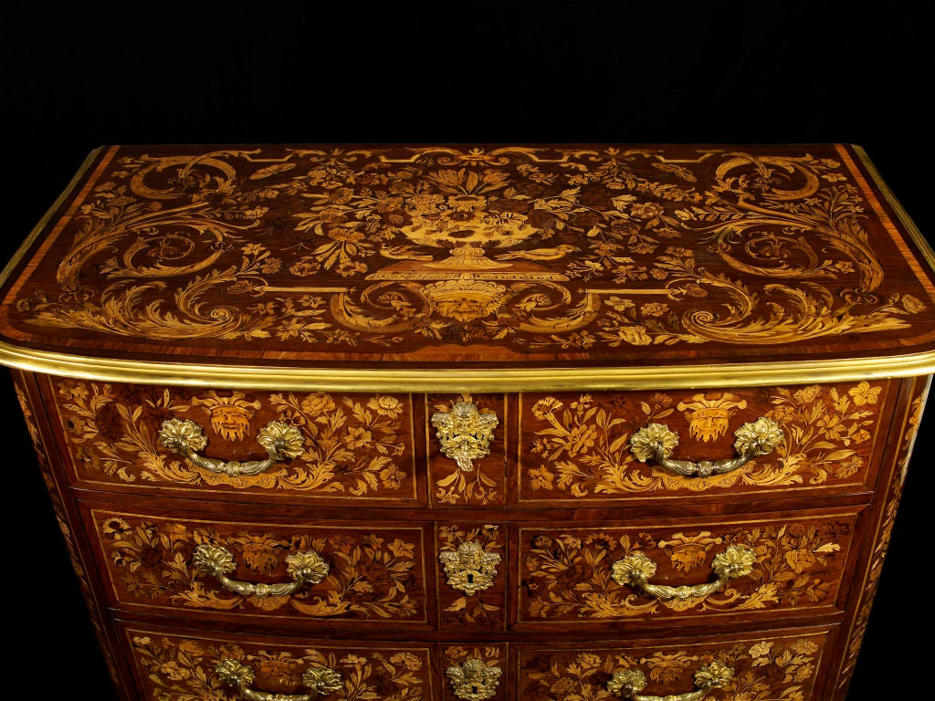 An important French Louis XIV period, ebonized, sycamore, walnut, and kingwood, cross banded, floral marquetry commode applied with gilt metal mounts.  The commode has a rounded rectangular top with molded brass edge, inlaid with a central floral