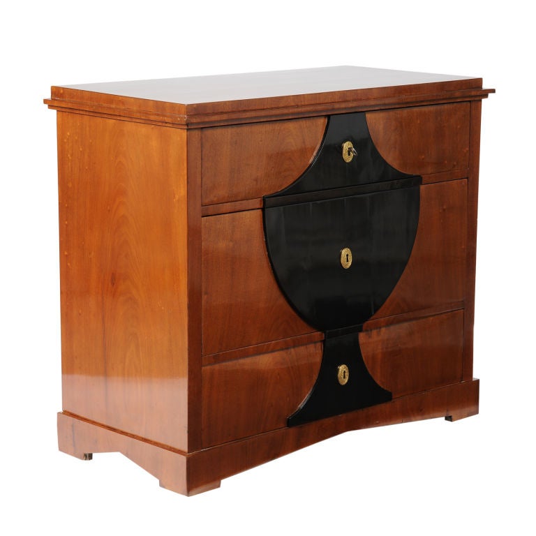 A Swedish Empire mahogany and ebonized commode, Circa 1800, with a overhanging rectangular top above three long drawers centered with an urn form relief, raised on block feet. The top drawer stamped GFT. Gustaf Foltern - Stockholm cabinet maker