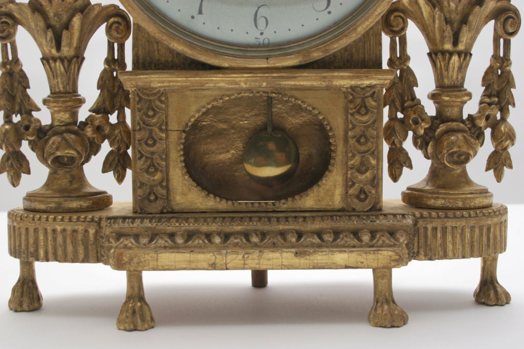 A Swedish Late Gustavian carved giltwood mantle clock, Late 18th Century, the white painted circular dial with Arabic  numerals and signed; Bjurman - Norrkoping, flanked by leaf carved finials with birds, surmounted with basket issuing flowers and