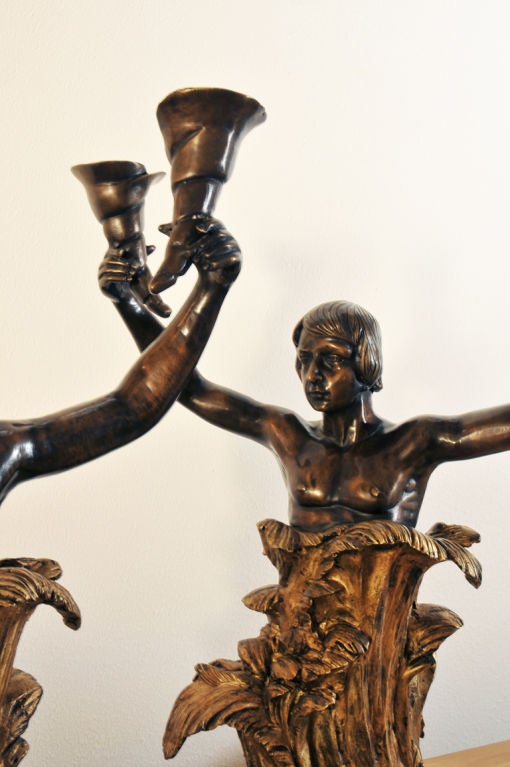 A pair of French Art Nouveau figural gilt bronze and patinated metal two-light candelabrum. The upper portions consist of a male figure which is completely enriched by a dark brown polished patina and the lower half containing a gilt bronze finish.