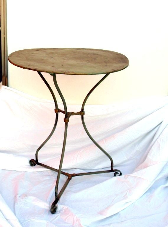 Typically seen at a bistro in Paris or other European cities, this cafe table is perfect in form and style.  With three curved metal painted legs on scroll feet and joined by an X-form stretcher that is highlighted with gold and supporting a