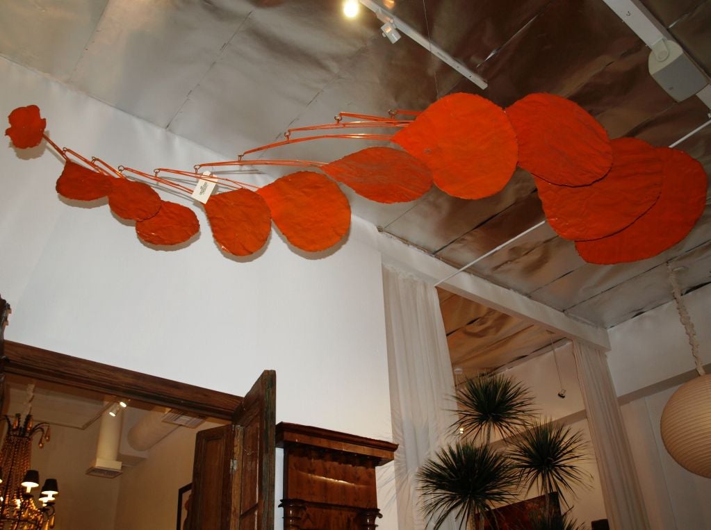 This large metal sculpture made of pounded steel and painted in a handsome rich reddish-orange color spans 9 feet wide when hanging at its widest point. Each of the nine perfectly balanced arms spin and glide through the air wherever it hangs. The