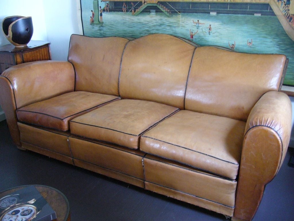 Leather Art Deco sofa. Tan leather with brown piping and wooden legs. Leather rip on top of sofa.
