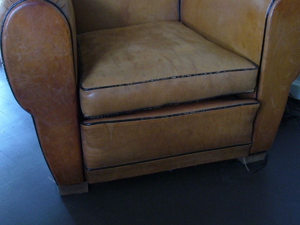 Pair of matching Art Deco club chairs. Tan leather with brown piping and wooden legs. Approx 1930-1940s. 