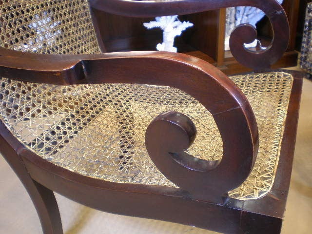 A pair of rare mahogany cane lolling chairs, with carved ears, rolled arms, and turned legs. These chairs maybe from Jamaica, or the Barbados, either way they are British Colonial Caribbean island fare.