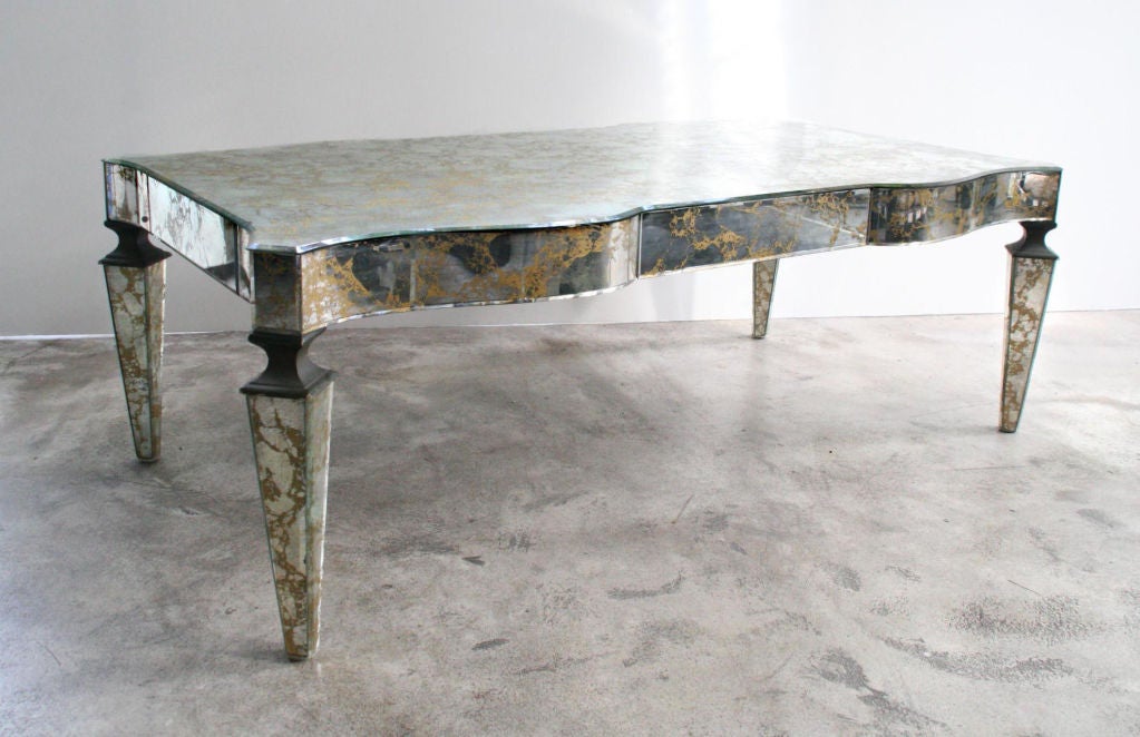 A striking low art deco mirrored coffee table, c. 1940's France. Gold veining throughout mirrors, elegant scalloped sides, tapered mirrored legs with painted wood joint details. Classic and elegant this table is a true beauty.<br />
<br