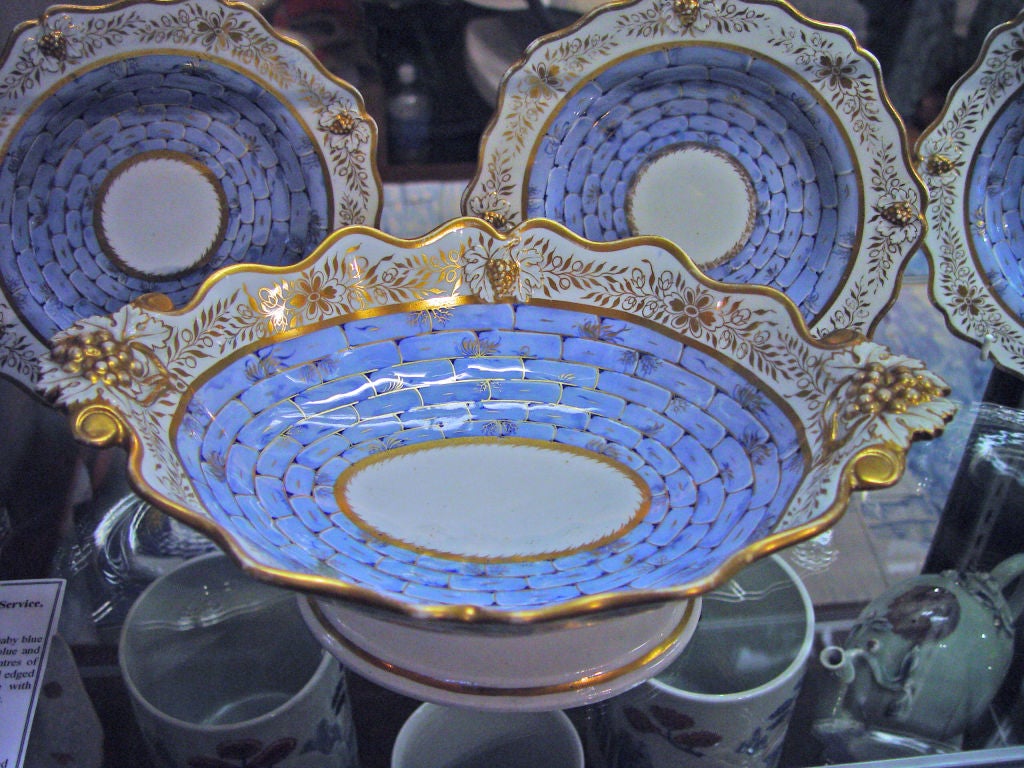 The dessert service with a moulded raised design of clusters of grapes decorated on the border with gilt flower heads within gilt bands.  The well decorated with blue stone blocks with gilt edges with a circular central panel with gilt leaf