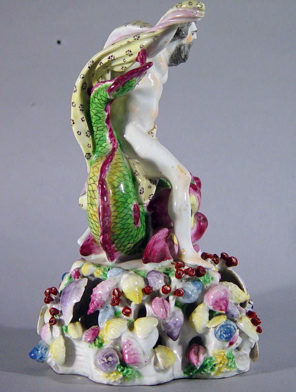 Neptune is depicted astride a multicoloured dolphin on an openwork shell base.  He wears a yellow cape held in his raised right hand which swirls around his body.  It is decorated with to different stylized purple flower-head designs.  The dolphin,