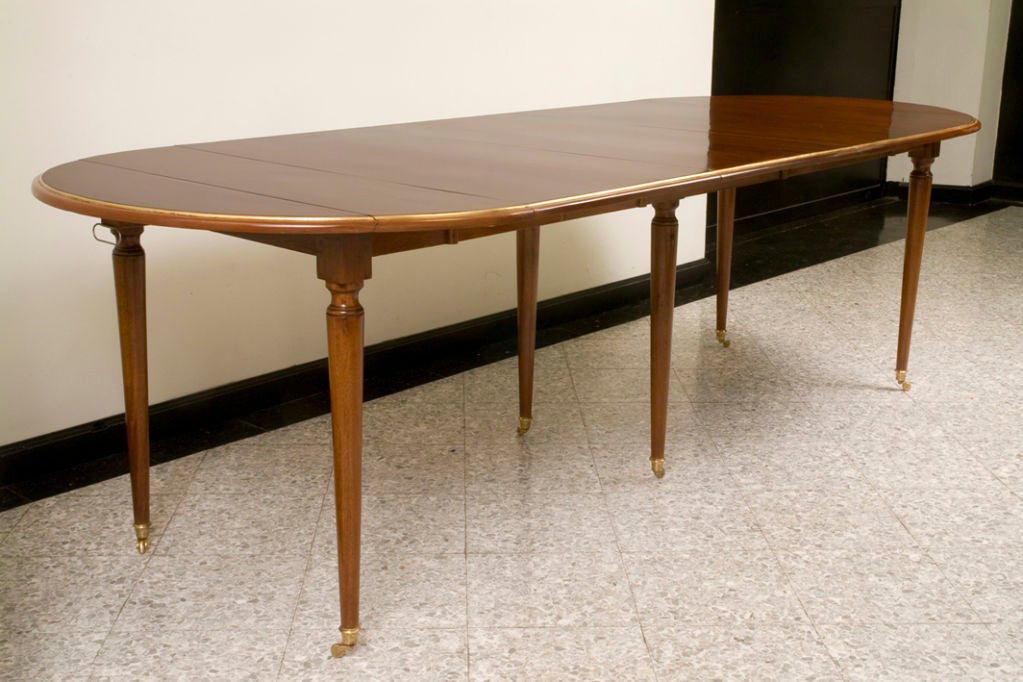 A Directoire style mahogany dining table with brass trim, six round tapering legs with brass sabots, three (modern) leaves.

Length 99