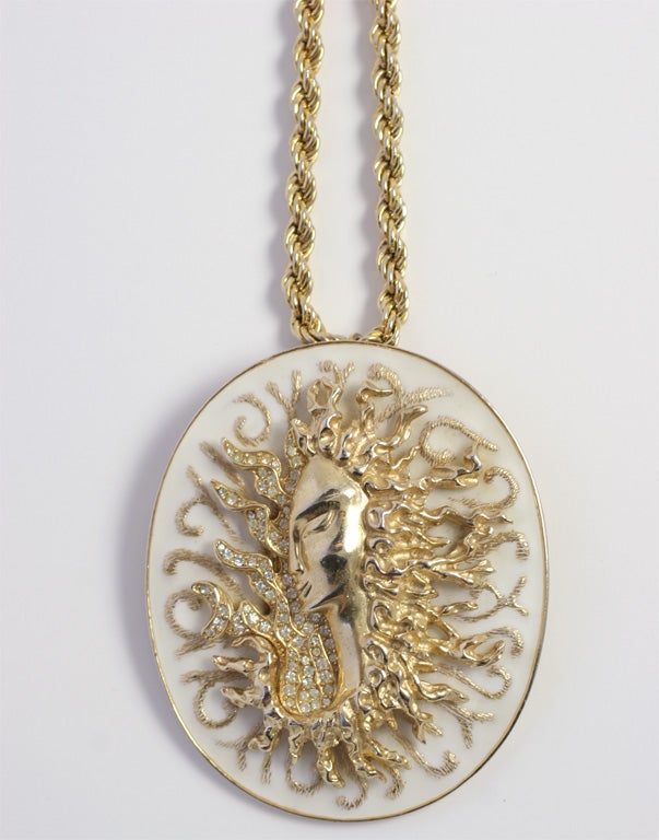 White enameled oval pendant with a crystal encrusted Medusa relief figure.
Chain is Monet.