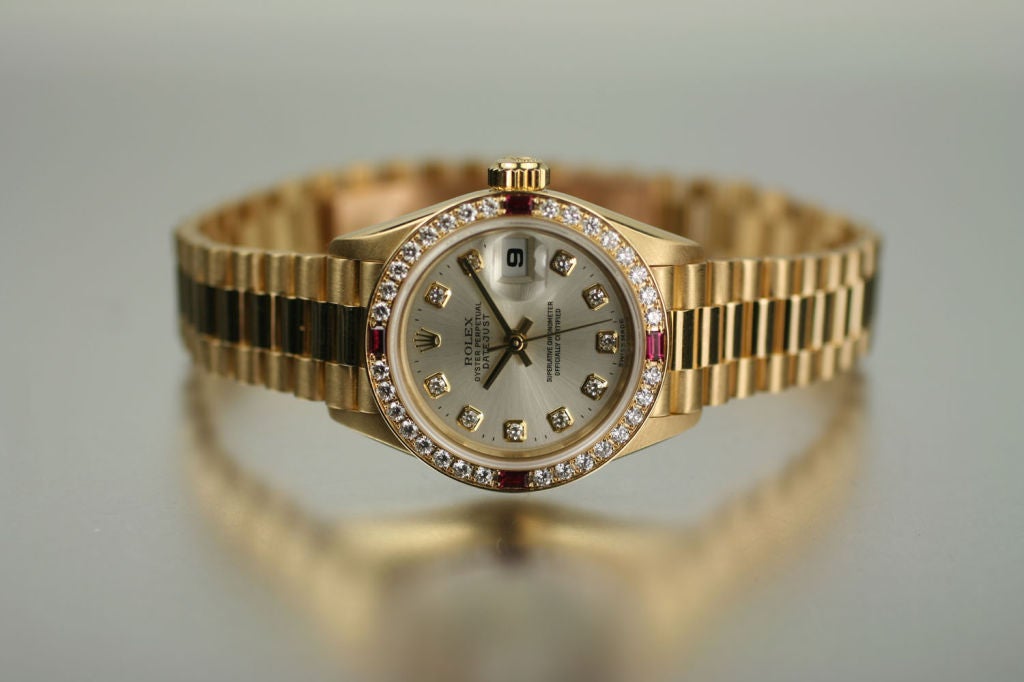 This beautiful yellow gold ladies’ Rolex Date Just watch has an automatic movement, serial reference # W, reference # 69068, silver dial, diamond markers, gold baton hands & sweep second hand, date aperture @ 3, sapphire crystal, 32-diamond bezel w/