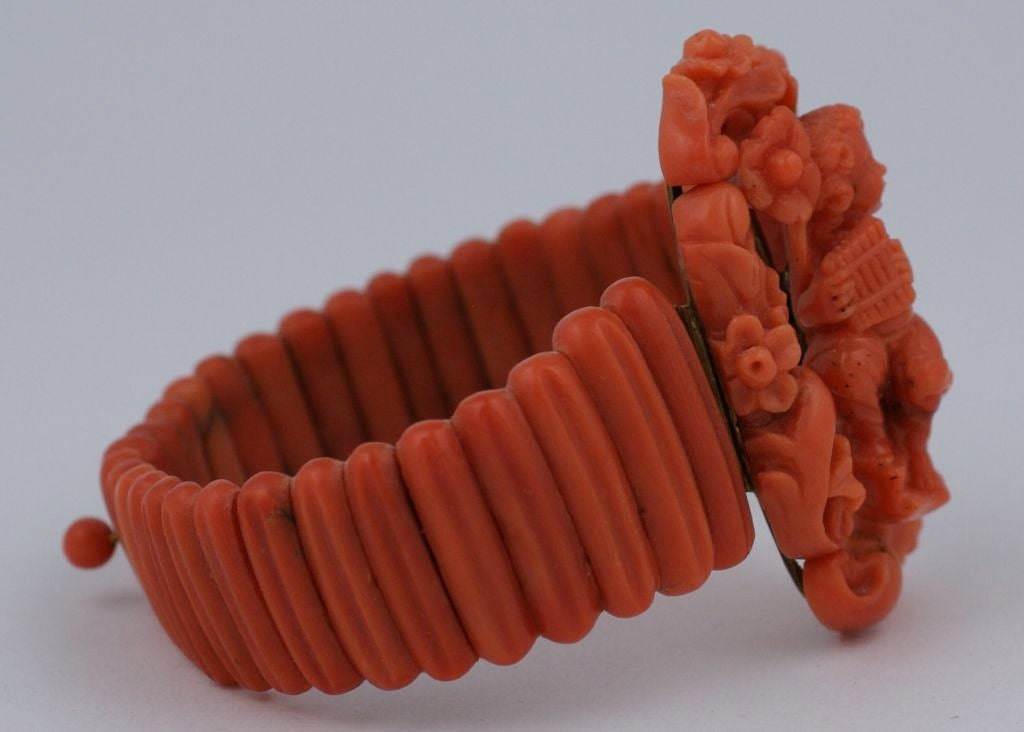 Wonderful 19th Century Coral cuff of a winged putti playing his flute. He sits surrounded in a garland of carved flowers and vines. Some of the fully carved 3D flowers are bolted onto the garland. Tapered coral "lonzenges" form the