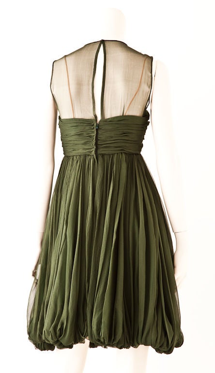 This Bruce Oldfield silk georgette cocktail dress is made of a beautiful shade of moss green. The top is sheer with a ruched bust/bra and has a empire waist. The dress has generous georgette fabric that softly drapes vertically  and finishes in a