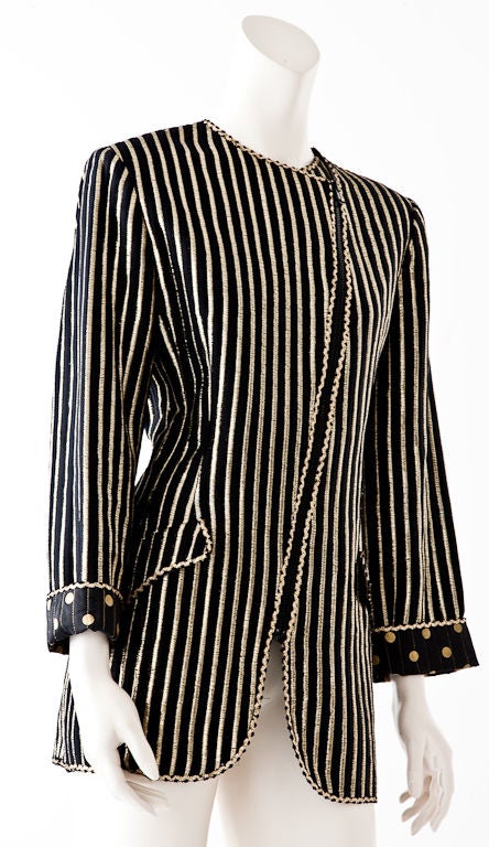 Geoffrey Beene gold lame on a black ground long, slightly fitted jacket with diagonally placed zipper closure. Exterior of jacket is in a stripe lame pattern and interior is a polka dot lame design. Jacket is edged in a gold trim and has two side