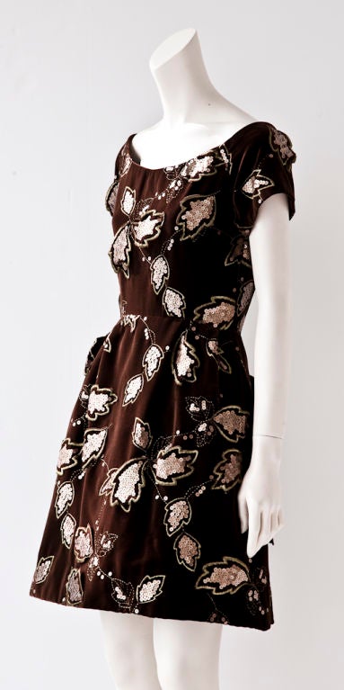 Scassi brown velvet cocktail dress with scoop neck and cap sleeve.<br />
Skirt is gathered at the hip and has a sculpted body. Dress has an embroidered leaf pattern embellishment with copper matte colored sequins mixed with coppery gold embroidery.