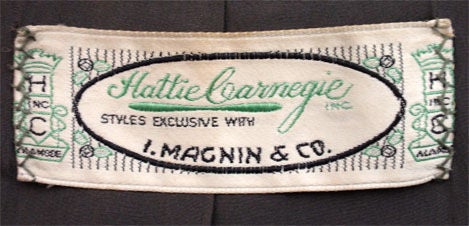 Il s'agit d'un ensemble jupe et veste deux pièces en laine grise par Hattie Carnegie avec I. Magnin and Company, de 1950. La veste a deux poches fendues sur le devant dans la couture princesse, quatre boutons noirs, une taille ajustée et des