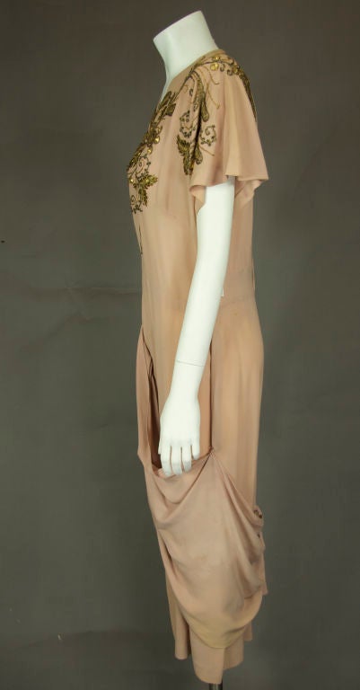 Putty pink crepe dress. Gold leather with beading metallic thread appliquéd around front bodice and back shoulders. Swag around skirt gathered at center front and center rear low back. Dolman sleeves. 
