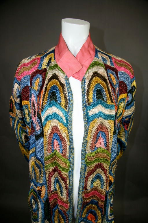 Circa 1925 crocheted coat. Pink, taupe, royal blue, light blue, bronze, brown burgundy, purple, orange, olive green, dark green, yellow, with pink grosgrain ribbon at neck, ending in an Aztec design at hem and cuffs. <br />
<br />
<br