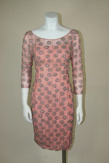 1960s couture hand-beaded fitted cocktail dress. Vertical lines with beaded circles with rhinestones in the center of the circles. Beaded lines wrap around the sleeves. Silk-tulle in a dusty pink as the outer lining. Silk-taffeta inset lining with