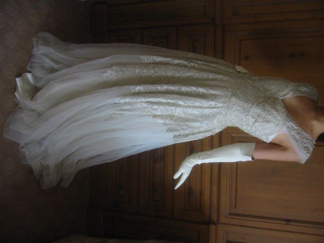 This stunning gown is made of white tulle and lace with gold thread woven through it. Designed with a sweetheart neckline with wide lace and tulle straps. The bodice is boned and hugs the torso. From the waist down the lace continues midway down the
