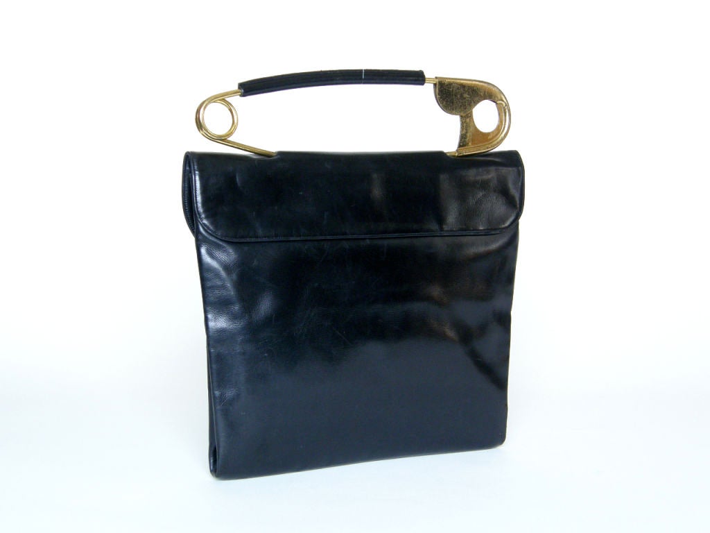 This iconic Koret bag has a touch of the surreal with the oversized safety pin handle. The body of the bag is made of black leather with the safety pin piercing the top flap. The interior is lined in black satin and has two slip pockets and a coin