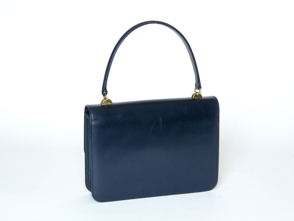 This navy leather Gucci handbag has a sleek and simple style. The bag has accordion fold gussets and two compartments inside. The interior is leather lined and has two slip pockets and one zippered pocket. You push the button to the side to release