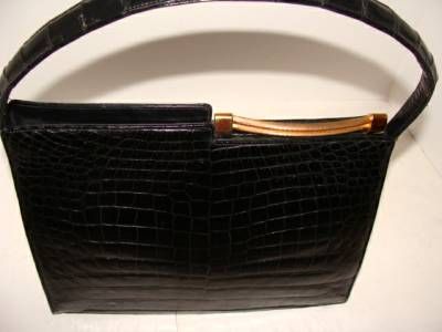 This black, center skin crocodile bag has a convex bottom which reinforces the curve in the unusual clasp.  The handle has excellent form and the majority of women can wear this over-the-shoulder and conveniently tuck under the arm. 

Large size