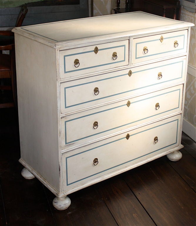In the style of William and Mary, a bun-footed chest of 2-over-3 graduated drawers in old 'ivory' paint with blue piped trim.