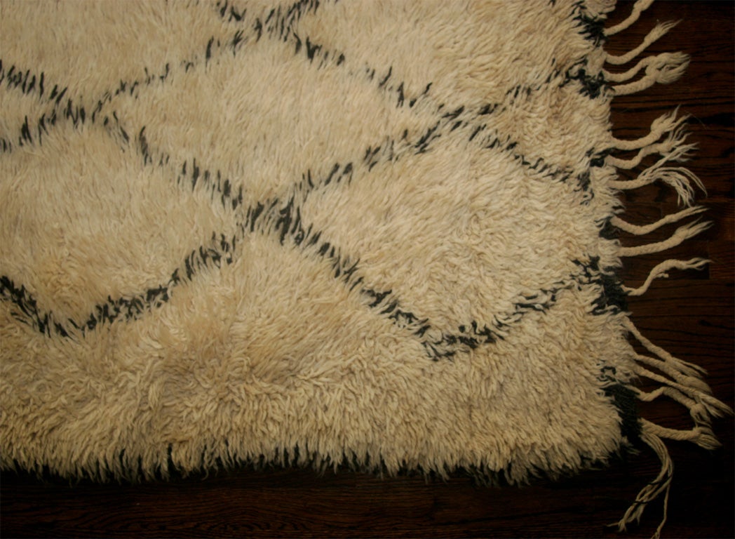 Shaggy Moroccan rug, off-white wool with a central diamond pattern. Fringed on one side.