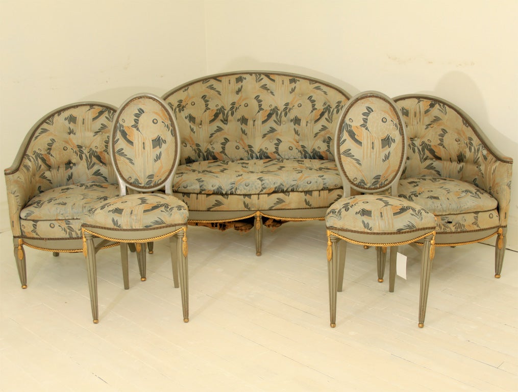 French Art Deco Salon Set: 2 side chairs, 2 armchairs and 1 settee. Wood in grey finish with carved details such as carved string and tassels partly gilded. Original Art Deco fabric in stylized fruit, plant and bird pattern, in diverse shades of