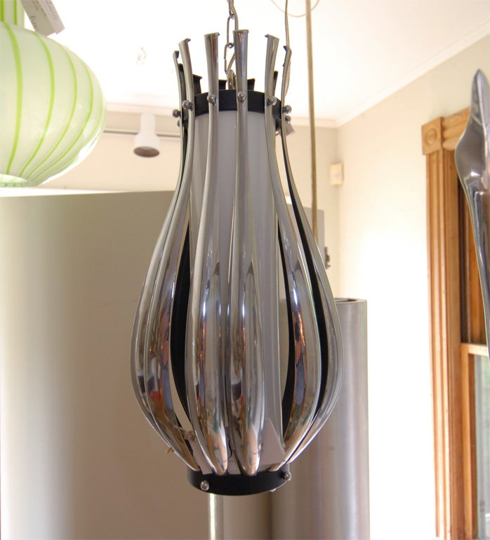Pendant fixture composed of multiple chrome slats arranged around opaque white glass cylinder.