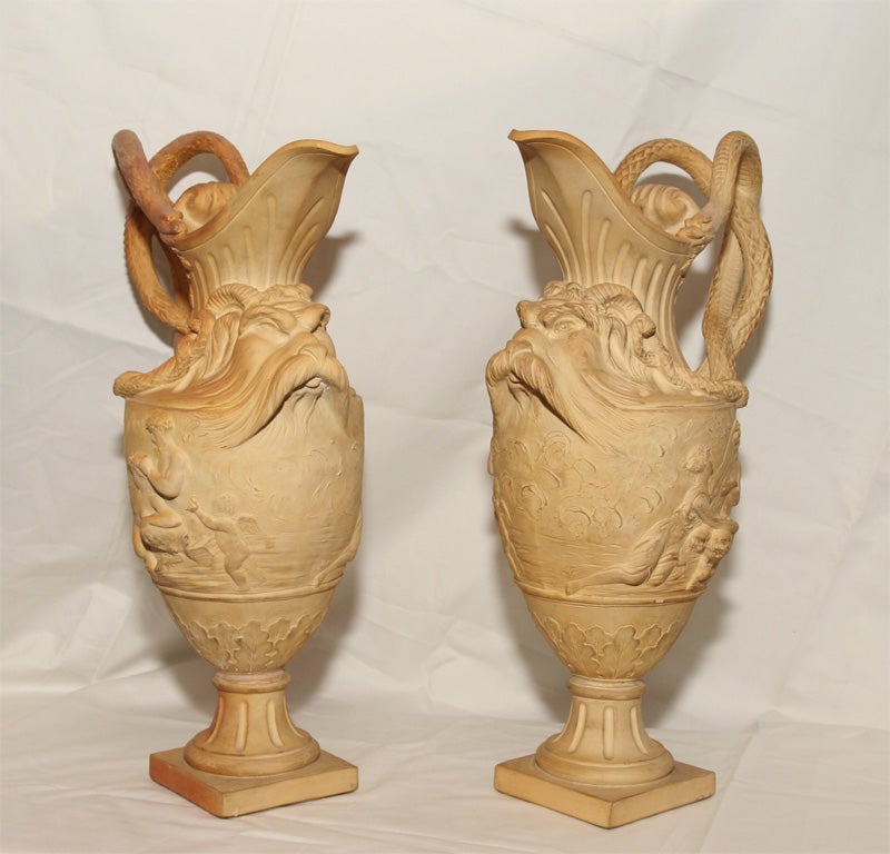 A pair of Bacchanalian terra cotta urns in the form of ewers with classical figures in relief, snake form handles and goat's head masks.