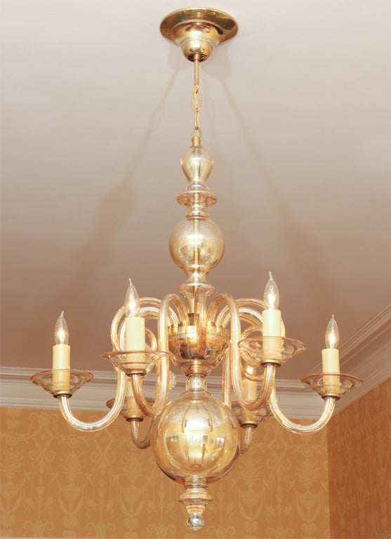 A lovely amber glass six-arm chandelier with a centre globe, six lights above round glass bobeches, and an additional six decorative arms. This piece is light and airy and has a whimsical quality about it. The amber glass gives it a pale gold tinge