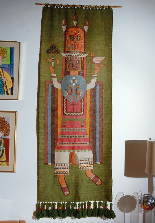 A large woven alpaca wool wall hanging tapestry labeled, Folklore by Olga Fisch, Quito Ecuador, depicting a woman in vibrant Pre-Colombian ceremonial attire detailed with metal bead work.