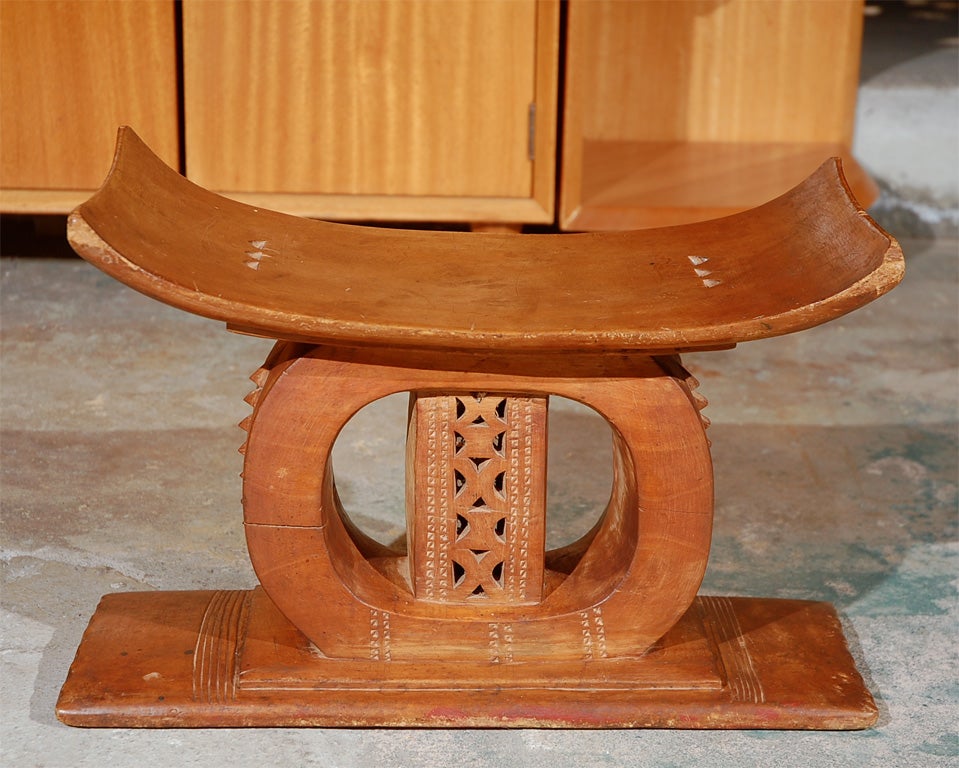 An early 20th century Ashanti stool in traditional form with a curved seat over a rounded support with a detailed interior set on a flat rectangular base. Of note on this piece is the spine of pyramid detailing on the outer edge of the support.