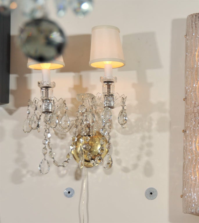 This cut crystal sconce with scrolled arms and tear drop beveled pendants recalls all of the elegant splendor of 1940s Hollywood. It has been with two lights, ivory silk shades, and polished brass fittings.  The fixture have been completely rewired