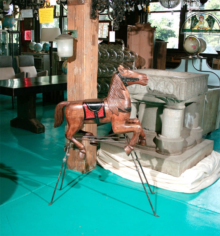 A carved wood carousel horse on an iron stand.