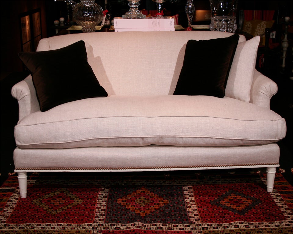 A white-painted canapé upholstered by our team in an off-white linen with nailhead trim with matching cushions, featuring a shaped back and curved armrests, and in the style of Maison Carlhian (velvet pillows not included).