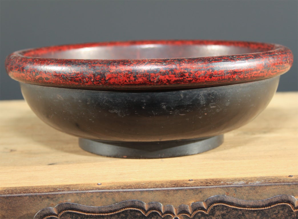 Japanese negoro lacquered wood bowl with heavy rolled rim. The rim and interior of the turned utilitarian bowl of red lacquer over an overall black lacquer on the body. The rim and interior heavily worn from use revealing the underlying black