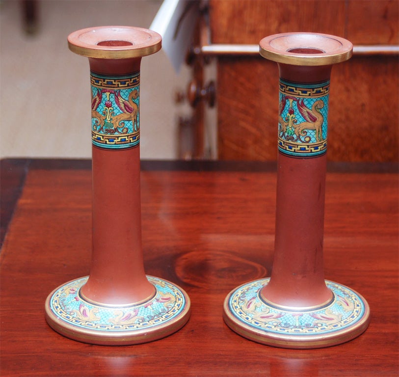 An unusual pair of Red Ware pottery candlesticks with an enamel 